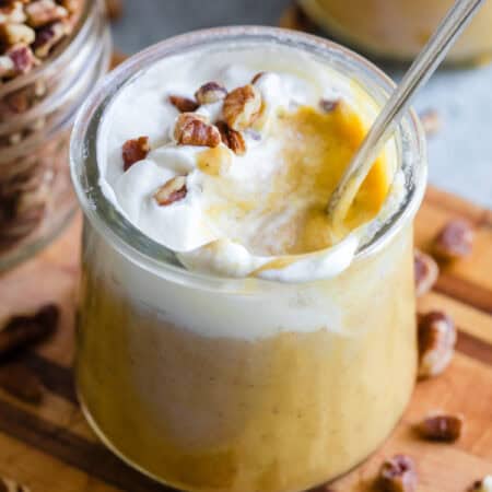 A spoon inserted into a glass jar of pumpkin pudding.