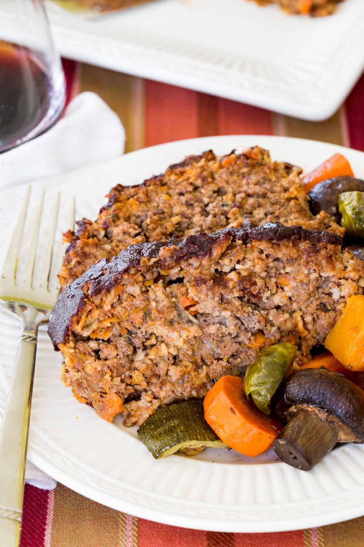 Slices of meatloaf on a plate with vegetables.