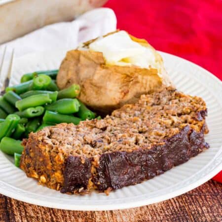 A slice of meatloaf with a baked potato and green beans.