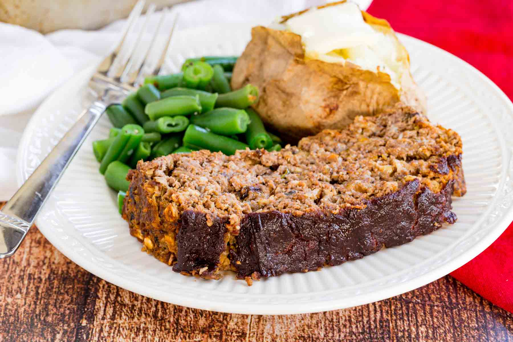 A slice of meatloaf with a baked potato and green beans.