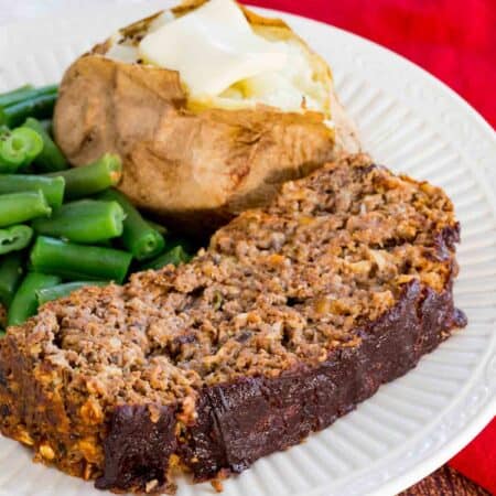 Meatloaf on a plate with a baked potato and green beans.