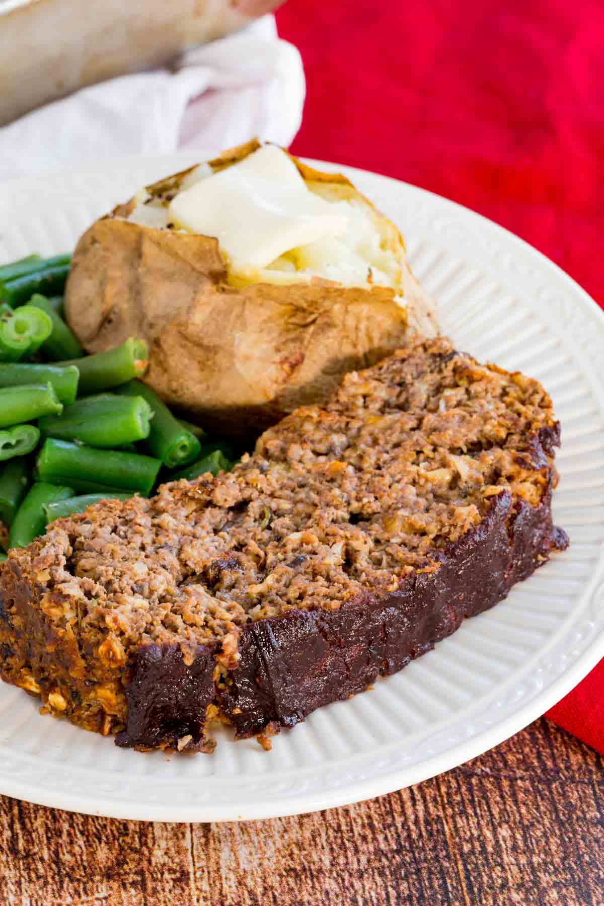 Meatloaf on a plate with a baked potato and green beans.