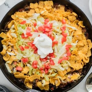 A cast iron pan of walking taco casserole topped with sour cream.