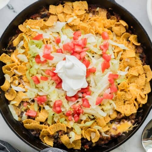 A cast iron pan of walking taco casserole topped with sour cream.