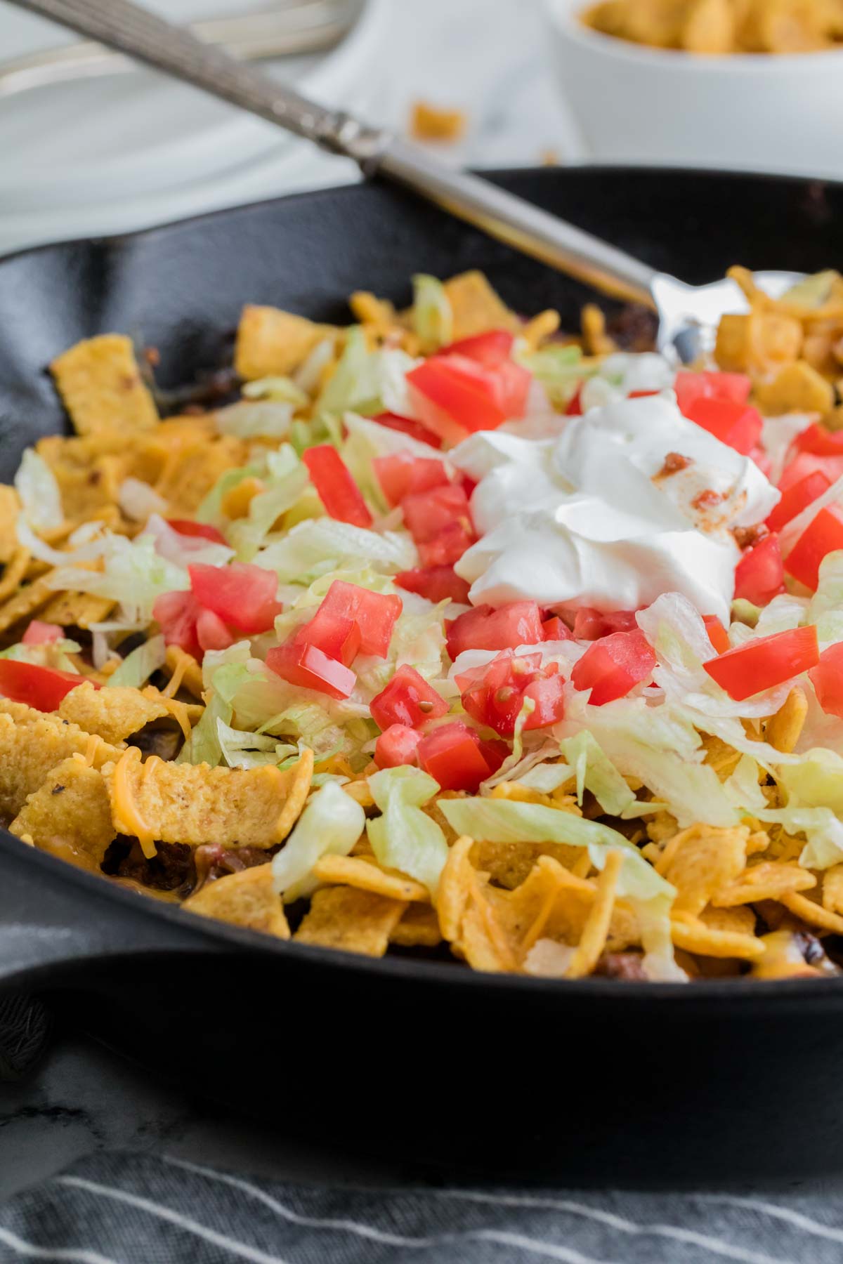 A spoon reaches into a cast iron pan of walking taco casserole.