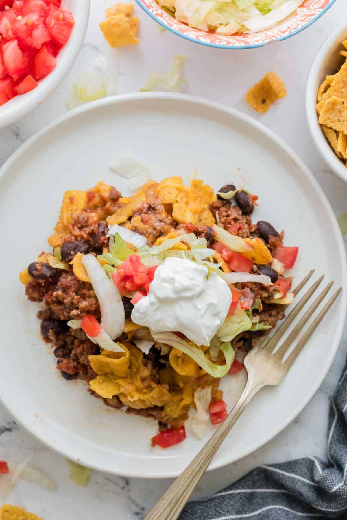 Sour cream tops a serving of walking taco casserole on a white plate with a fork.