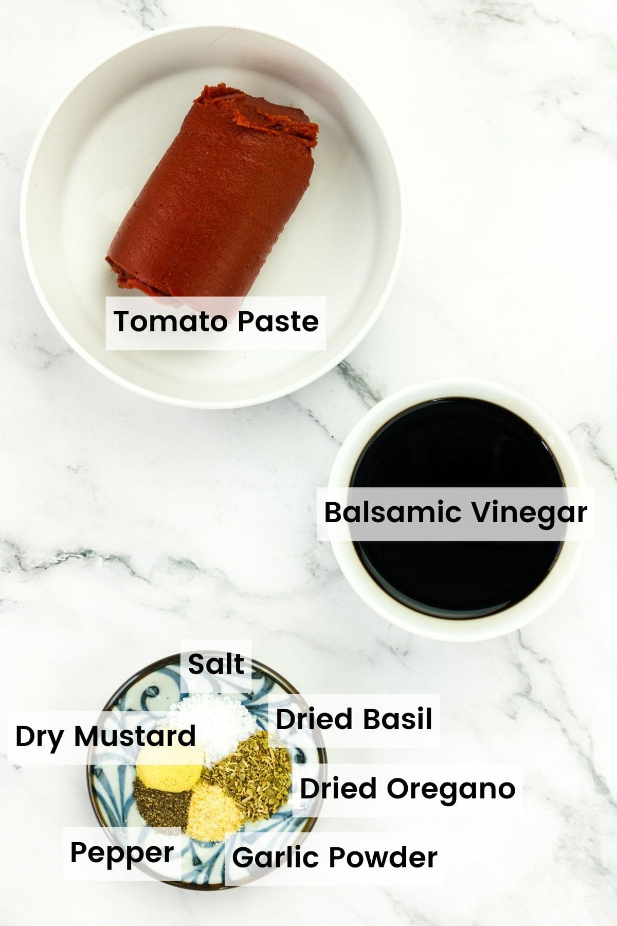 Balsamic ketchup ingredients portioned out with text labels including tomato paste, balsamic vinegar, dry mustard, dried oregano, fried basil, salt, and pepper.