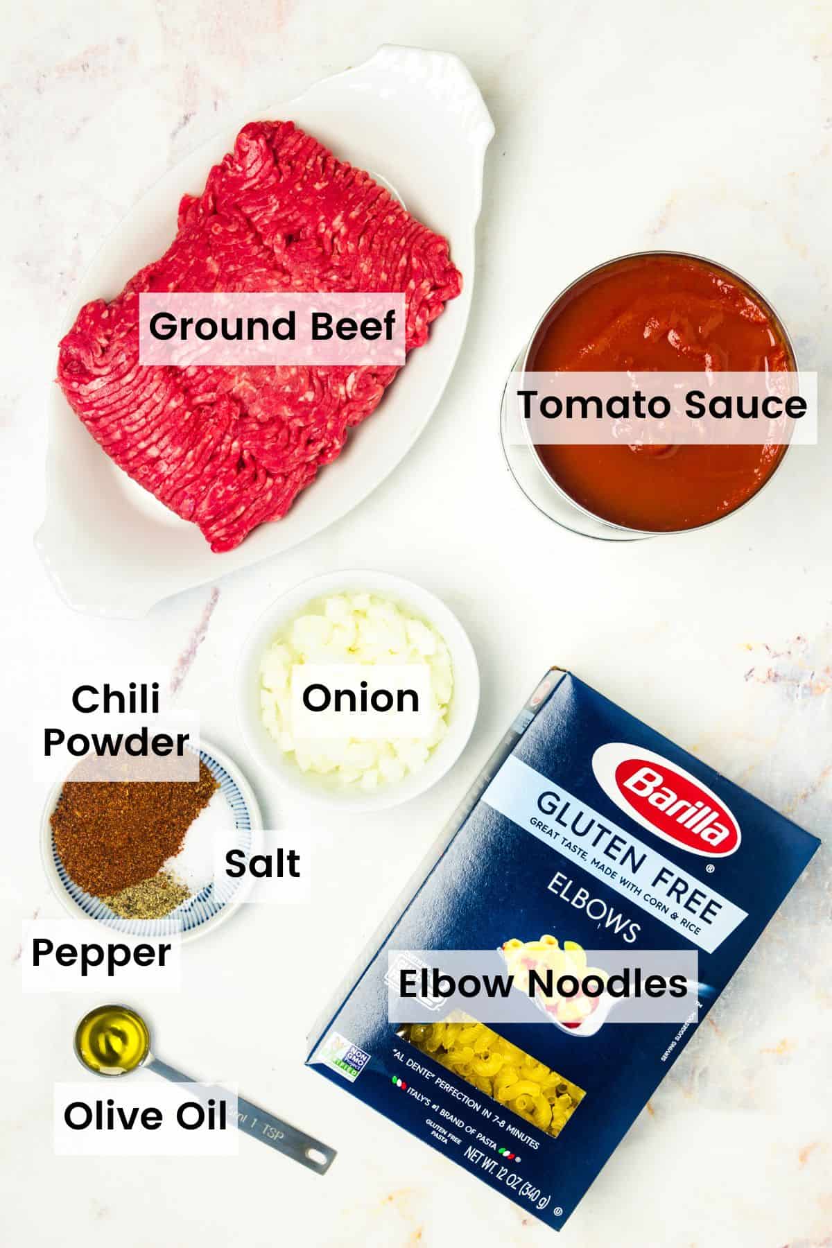 The ingredients for beefaroni are shown with text labelst: ground beef, onion, garlic, gluten free elbows, tomato sauce, olive oil, chili powder, salt and pepper.