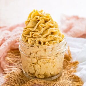 A glass jar with pale orange pumpkin frosting on a light orange napkin.