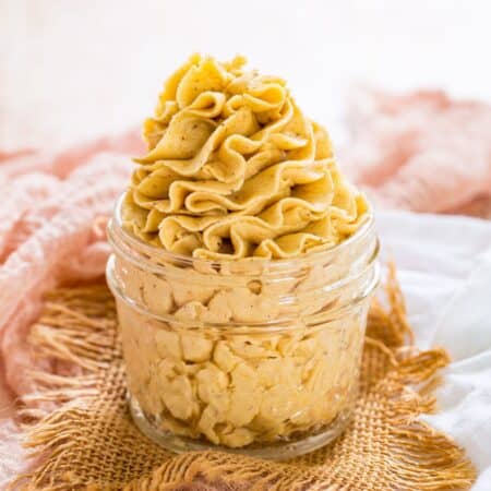 A glass jar with pale orange pumpkin frosting on a light orange napkin.