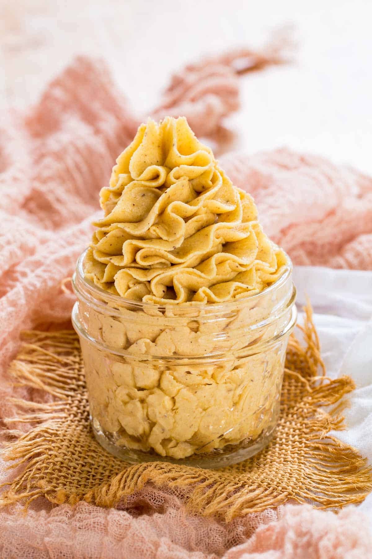 A glass jar with pale orange pumpkin frosting on a light orange napkin.