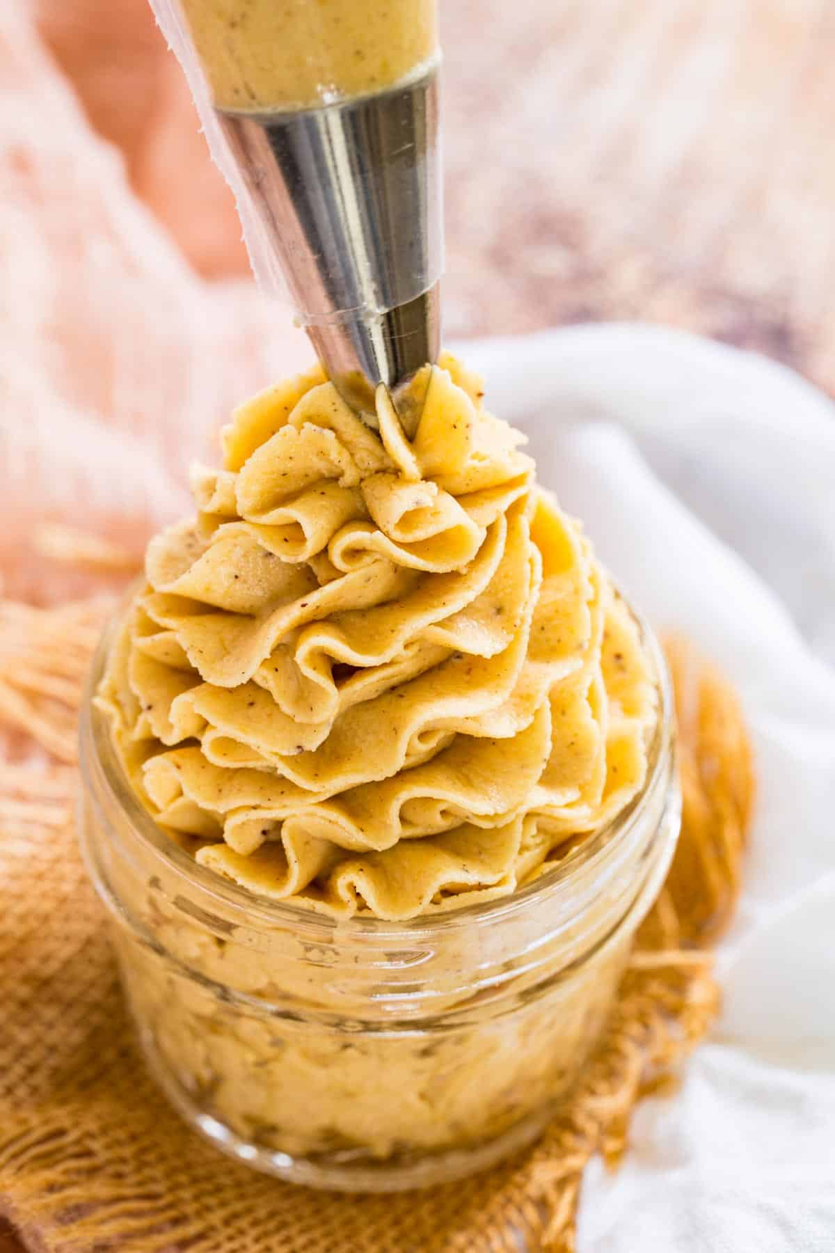 A piping tip pipes orange pumpkin frosting into a glass jar.