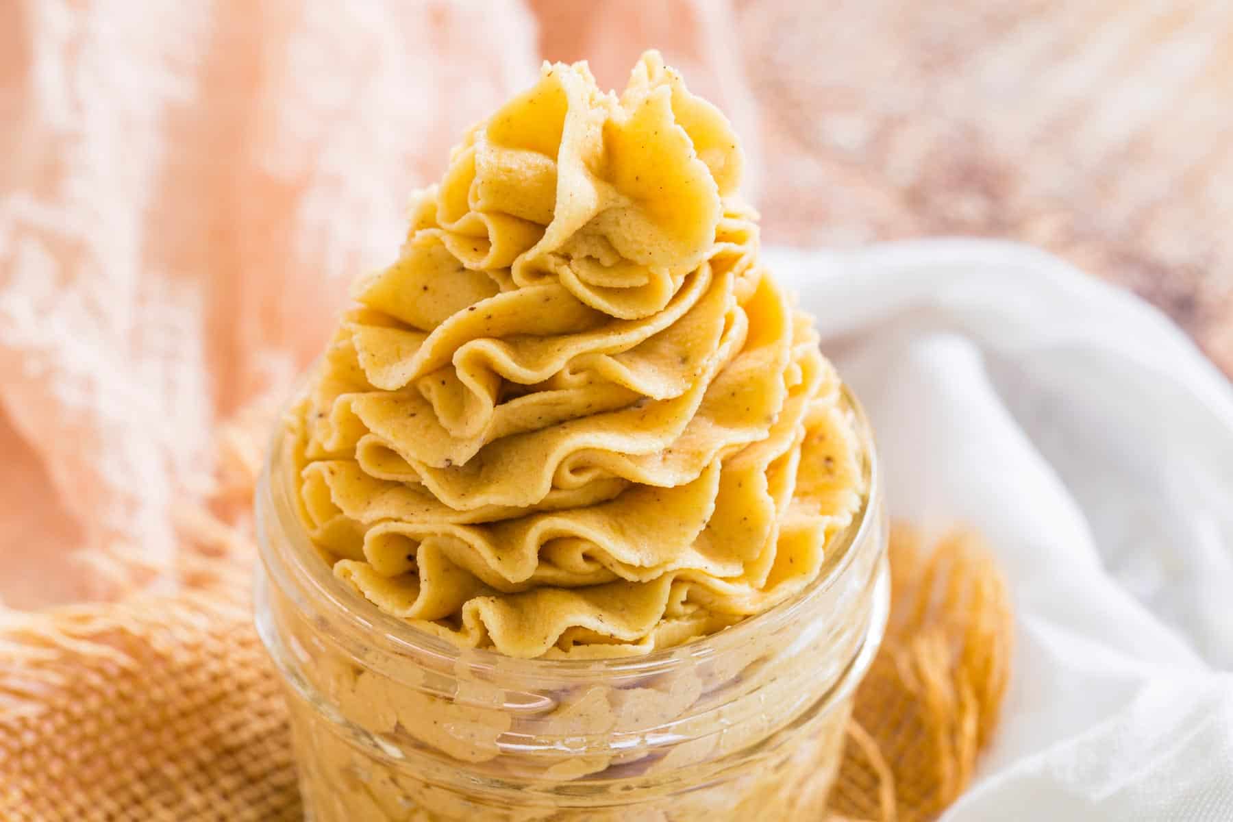 Pale orange pumpkin frosting is piped decoratively in a jar.