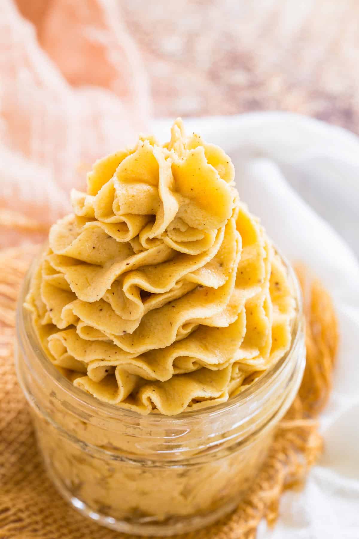 Pale orange pumpkin frosting is piped decoratively in a jar.