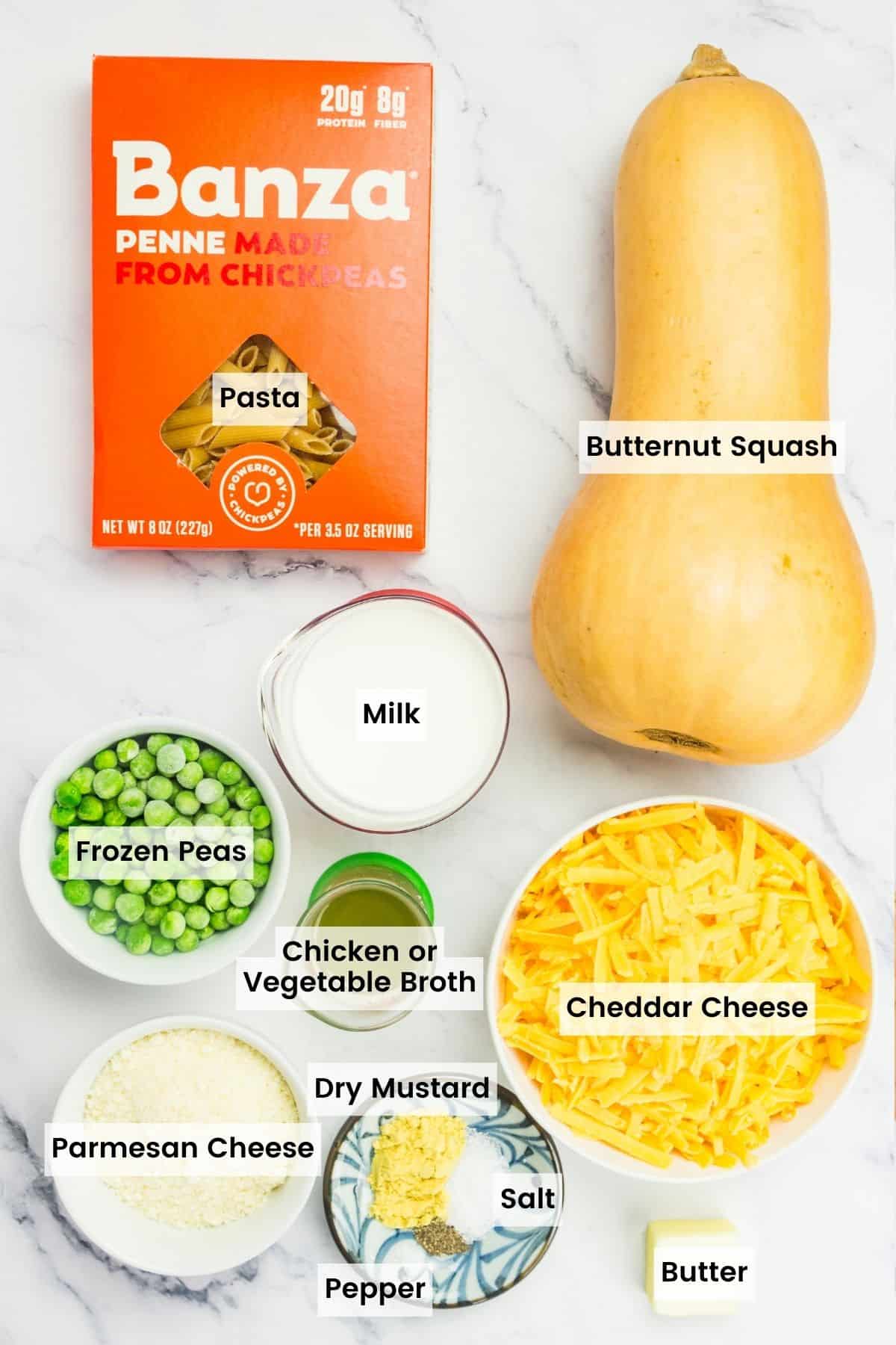 Ingredients for butternut squash mac and cheese portioned out with text labels including pasta, butternut squash, milk frozen peas, broth, cheddar cheese, parmesan cheese, dry mustard, salt, pepper, and butter.