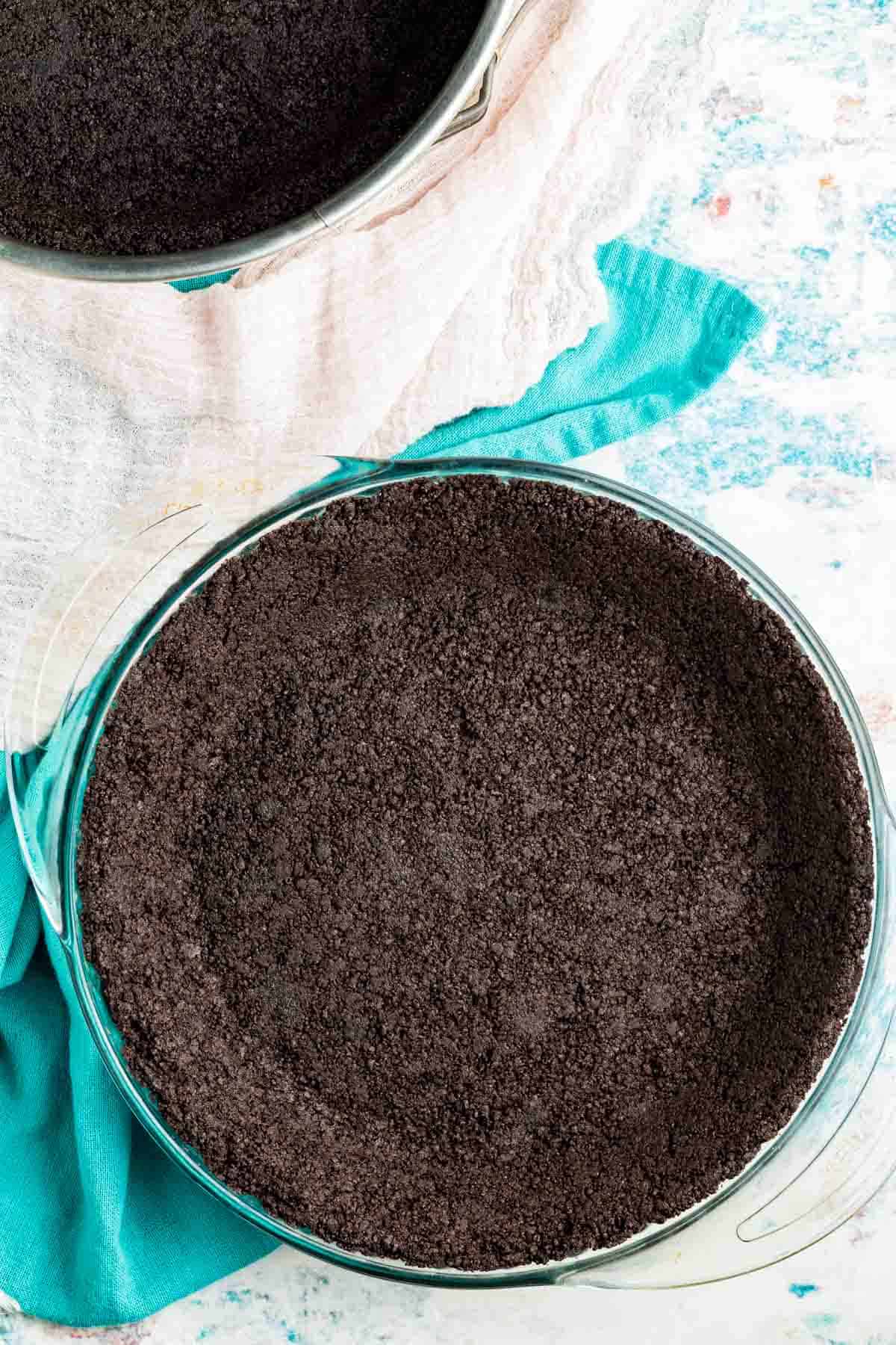 A springform pan with an oreo pie crust on a blue towel.