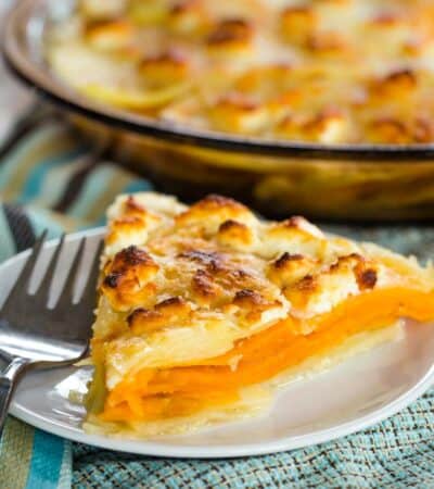 A lightly browned piece of goat cheese sweet potato gratin in front of a pan of gratin.