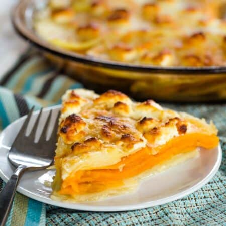 A lightly browned piece of goat cheese sweet potato gratin in front of a pan of gratin.