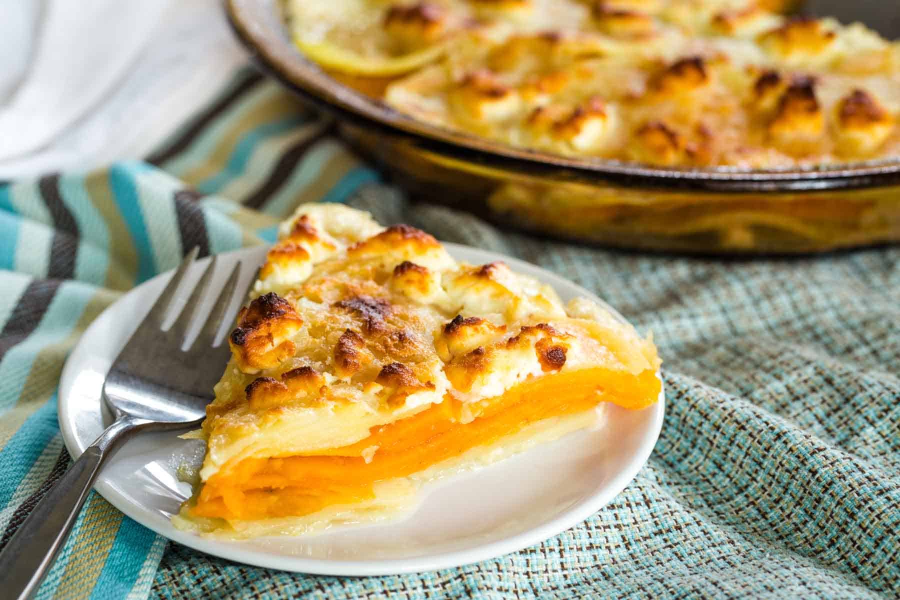 A lightly browned piece of goat cheese sweet potato gratin in front of a pan of gratin.