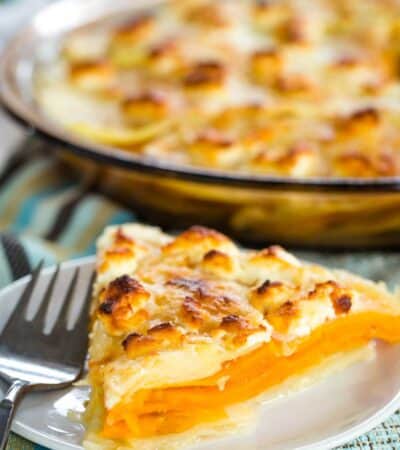 A lightly browned piece of goat cheese sweet potato gratin in front of a pan of gratin.