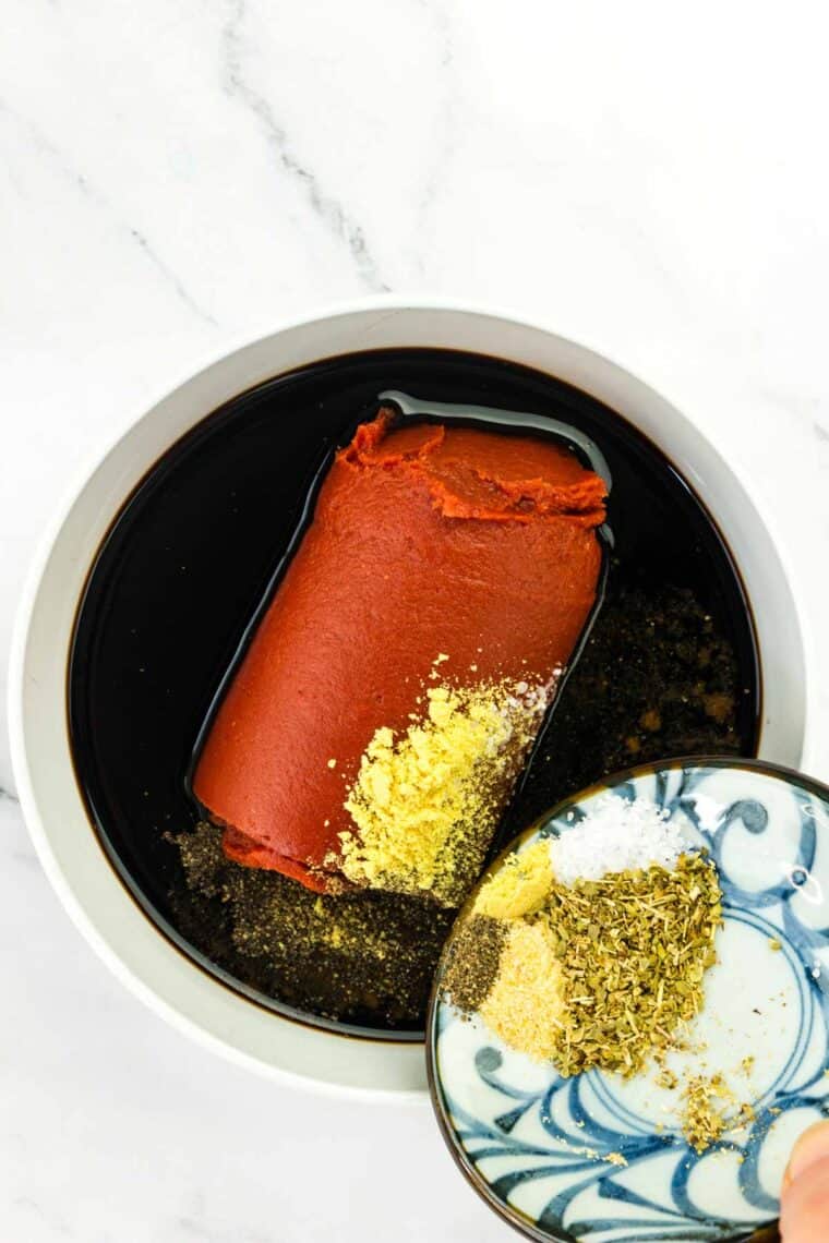 Seasonings being added to the tomato paste and balsamic vinegar in a bowl.