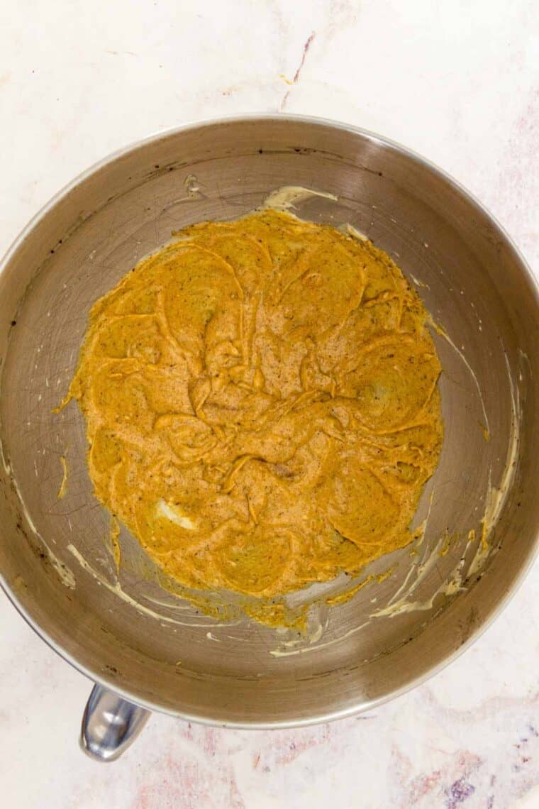 Powdered sugar is added to the pumpkin frosting in a bowl.