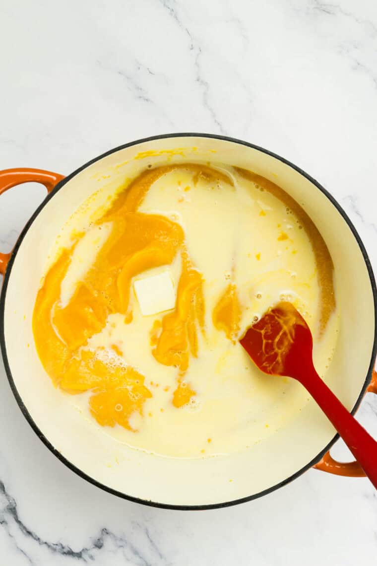 Milk and butter being stirred into butternut squash puree in a pot.