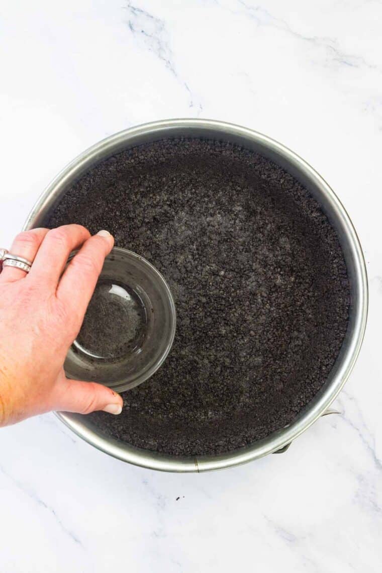 Using a glass to press oreo pie crust into a springform pan.