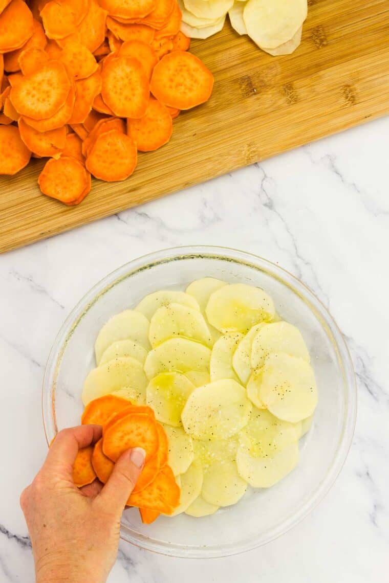 Adding sweet potato circles to a dish of sliced potatoes.