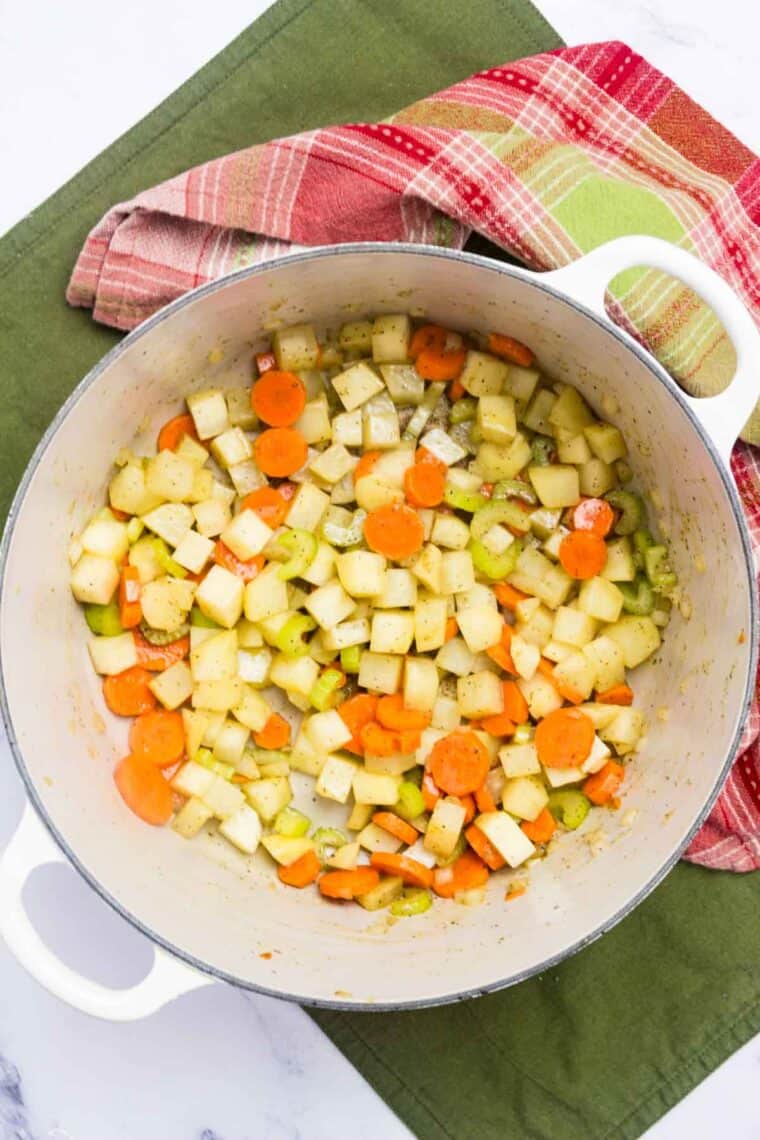 Carrots, celery, and onion cook in a pot.