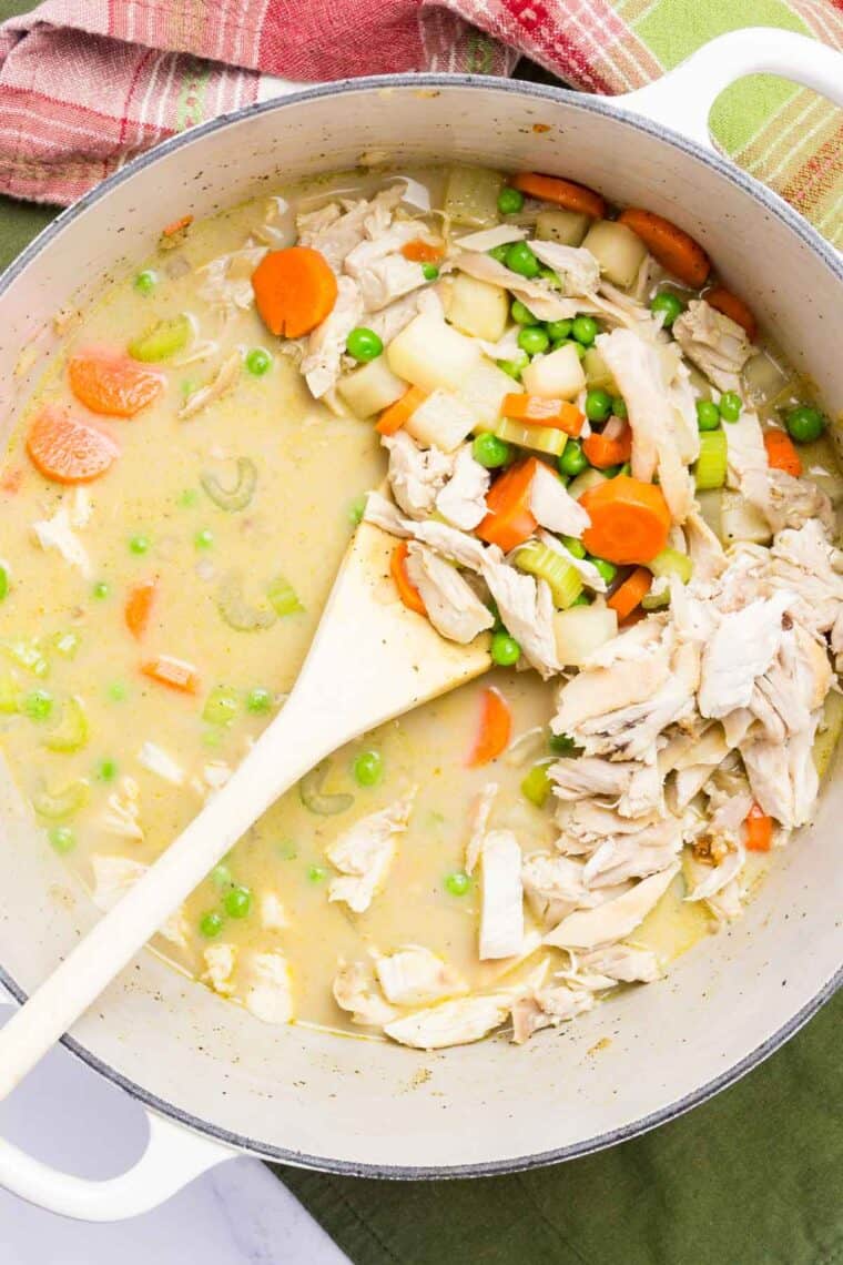 A wooden spoon stirs turkey and vegetables in broth.