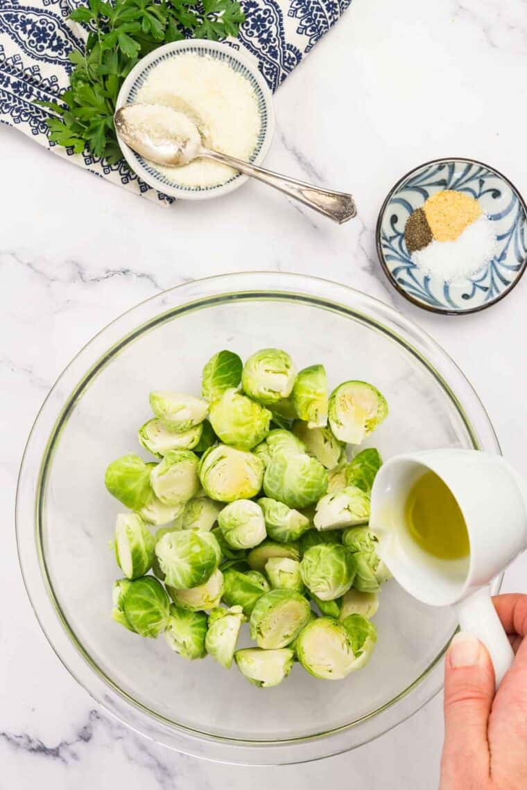 Oil is poured onto Brussels sprouts in a bowl.