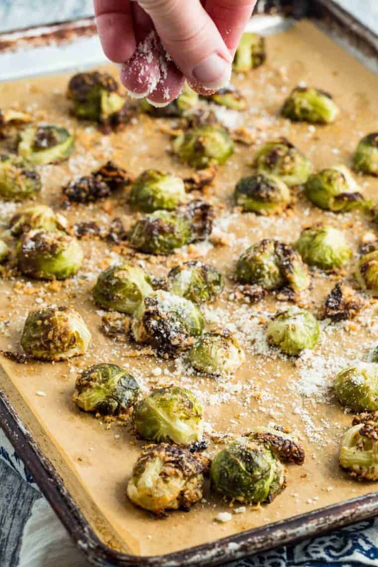 Sprinkling cheese on a pan of roasted Brussels sprouts.