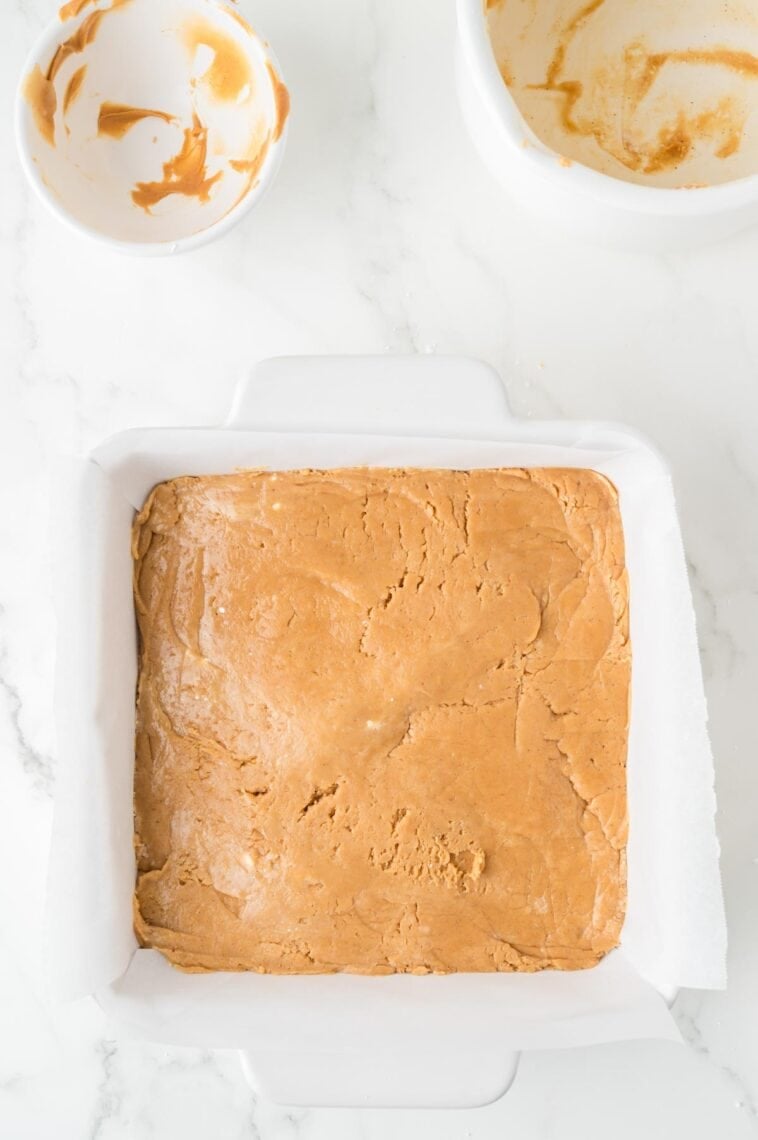 Peanut butter fudge mixture is pressed into a baking dish.