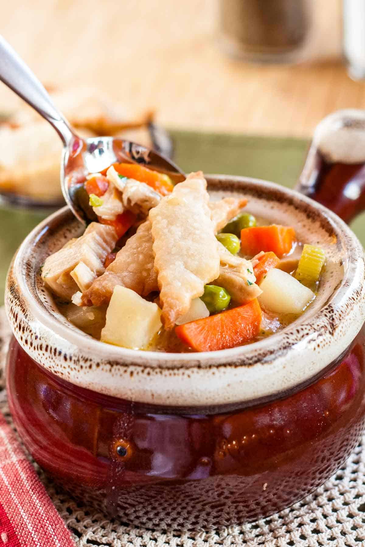 A heaping spoonful of leftover turkey soup above a bowl.