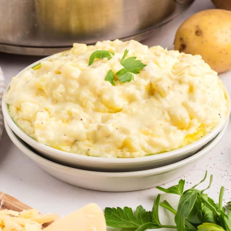 A bowl of parmesan mashed potatoes with parsley garnish.