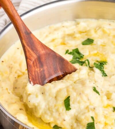 A wooden spoon stirs a pot of parmesan mashed potatoes.