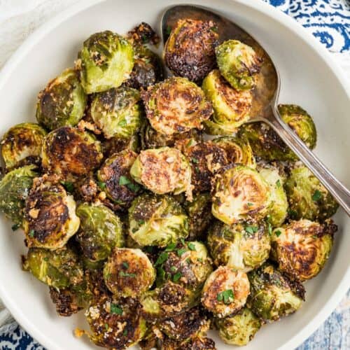 A serving spoon in a bowl of roasted Brussels sprouts with parmesan.