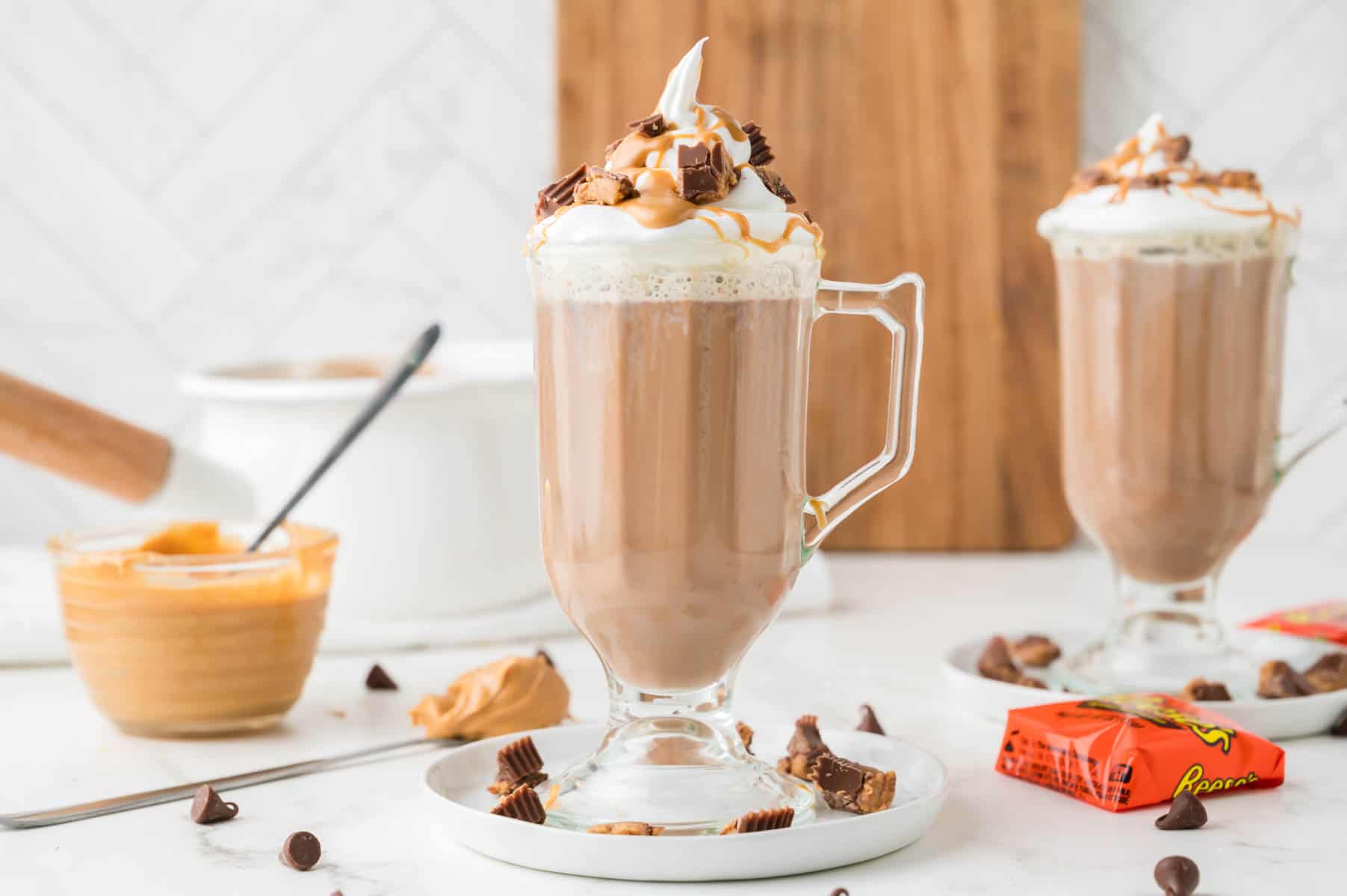 Glasses of peanut butter hot chocolate with chopped reese's around them.