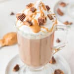 Chopped reese's and peanut sauce top a glass of peanut butter hot chocolate.