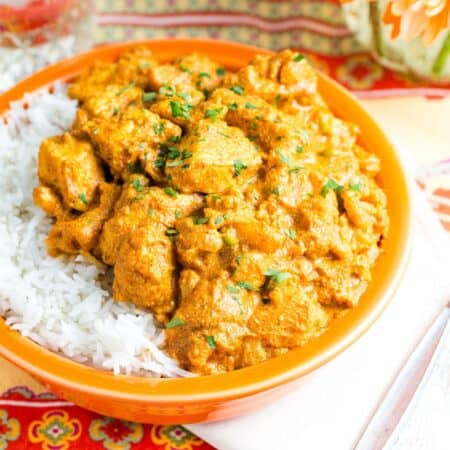 An orange bowl of chicken curry served over basmati rice.