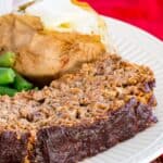 A slice of meatloaf on a plate with a baked potato and green beans with text overlay that says "Roasted Vegetable Balsamic Meatloaf".