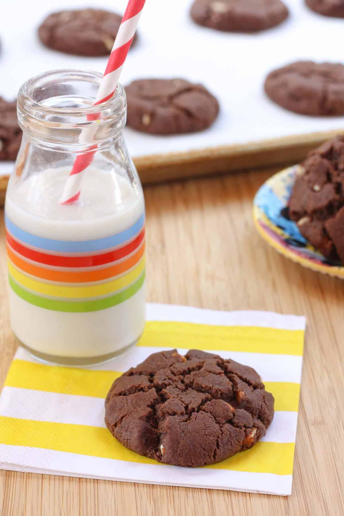 A glass of milk with a straw and a flourless chocolate almond cookie on a napkin.