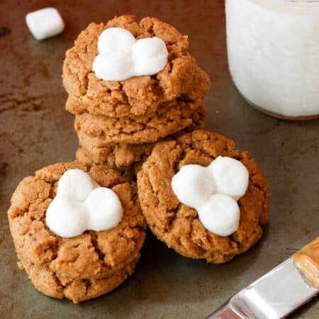 A glass of milk next to marshmallow-topped fluffernutter cookies.