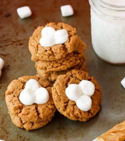 A glass of milk next to marshmallow-topped fluffernutter cookies.