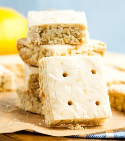 A lemon shortbread cookie turned on its side rests against a stack of cookies.