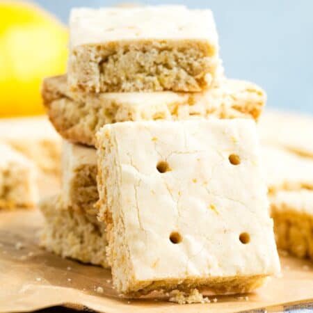 A lemon shortbread cookie turned on its side rests against a stack of cookies.
