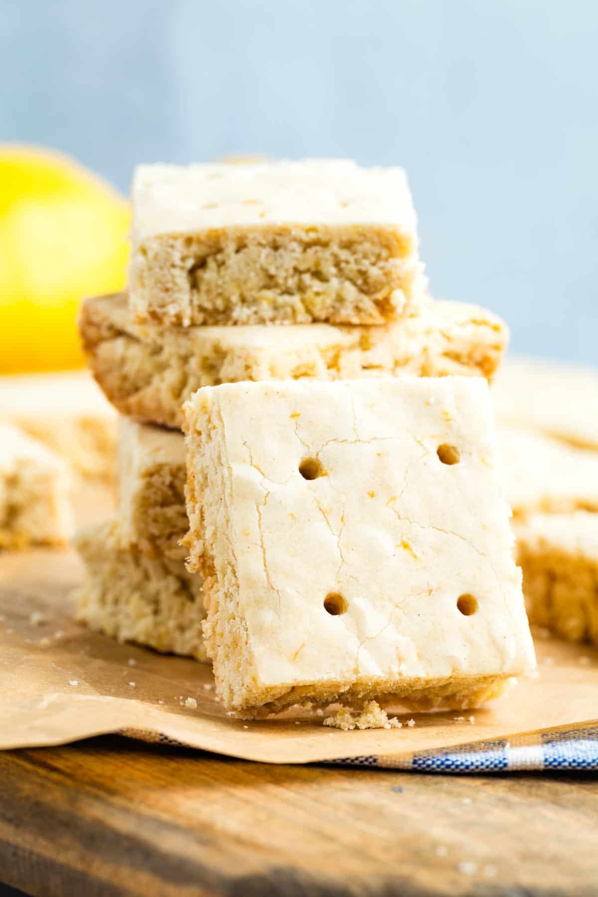 A lemon shortbread cookie turned on its side rests against a stack of cookies.