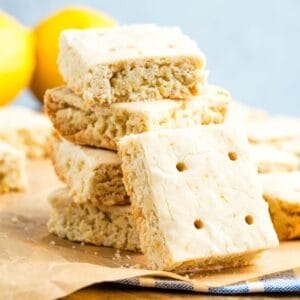 A lemon shortbread cookie turned on its side rests against a stack of cookies.