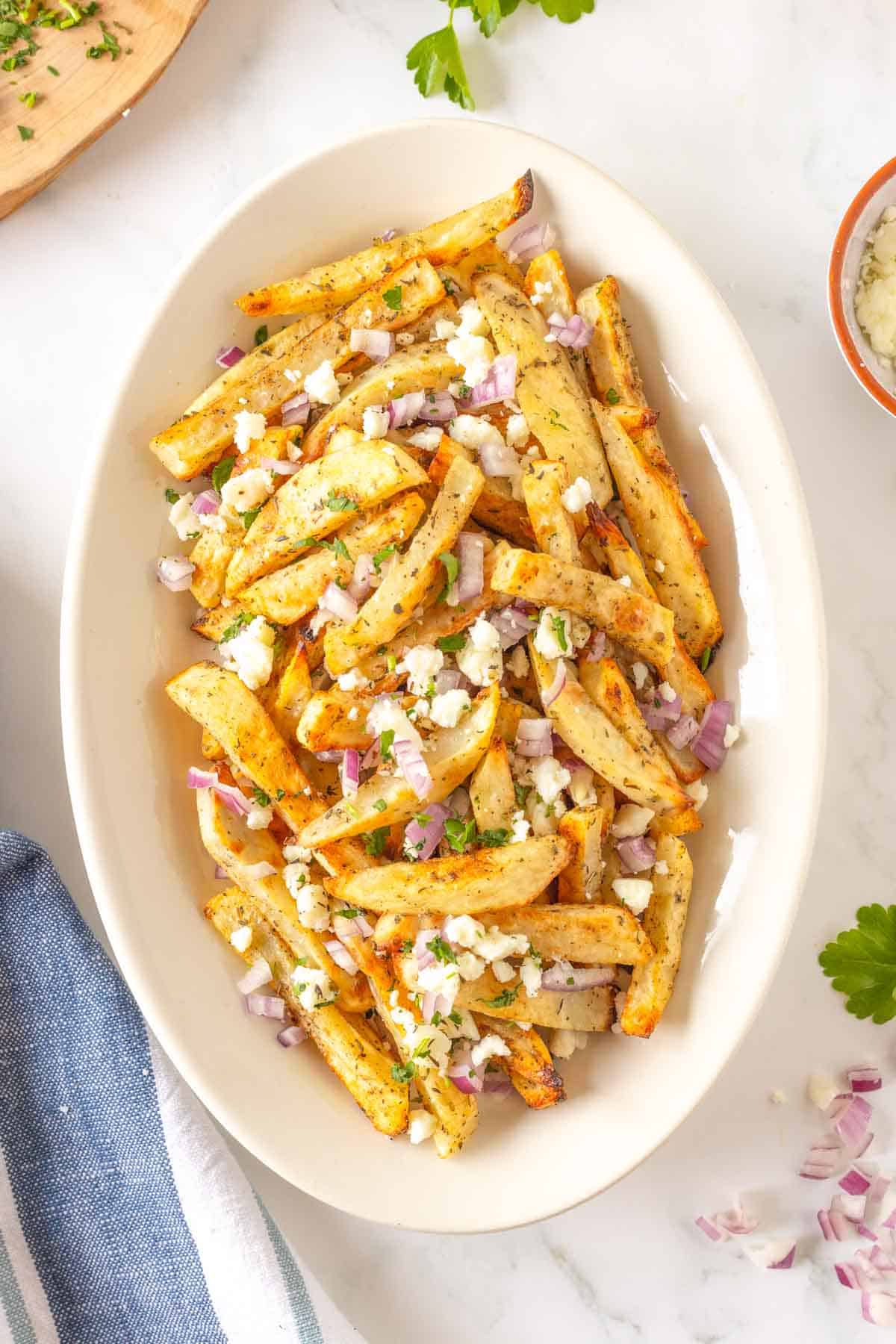 An oval platter filled with feta-topped Greek fries.